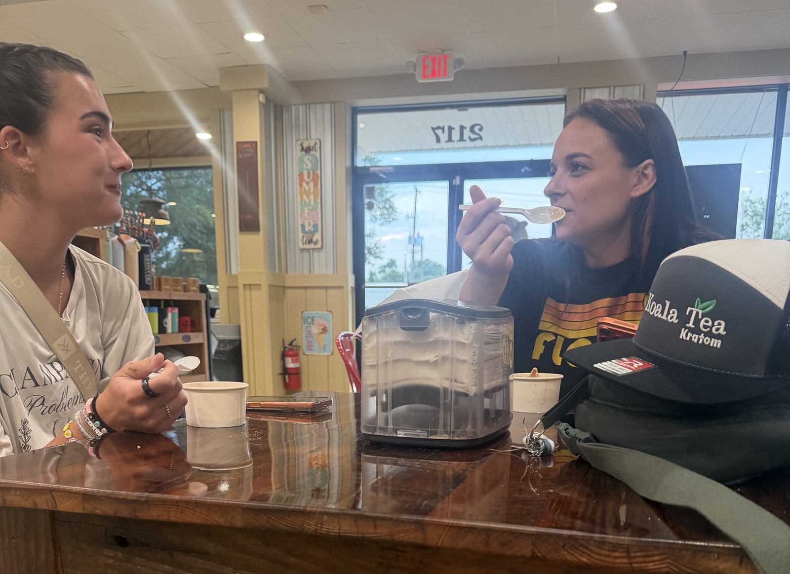 Sophia and Avery sitting across a wooden table with cups of water ice, mid-conversation